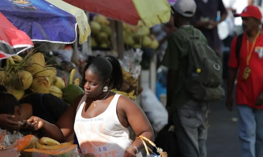 A woman buying fruit at a busy market stall piled with coconuts